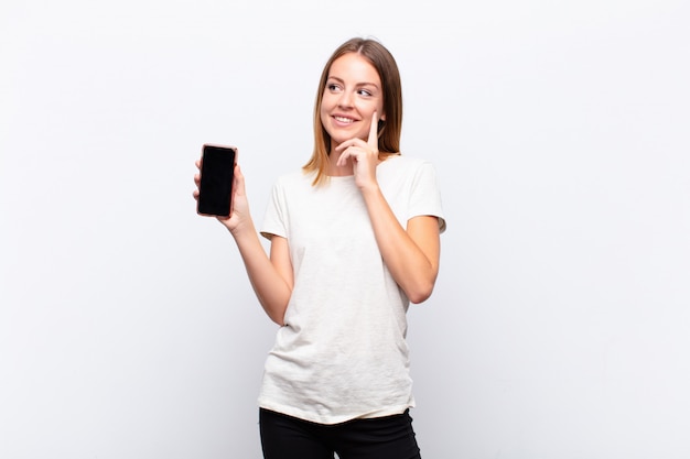 Niña con teléfono inteligente sonriendo alegremente y soñando despierto o dudando