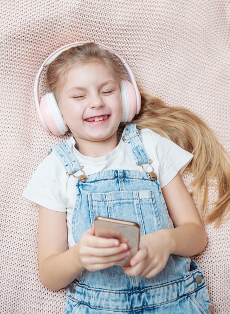 Niña con teléfono móvil escuchando música mientras está acostado en la cama