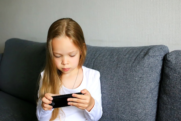 Niña con un teléfono móvil y se sostiene en sus manos y lo mira.