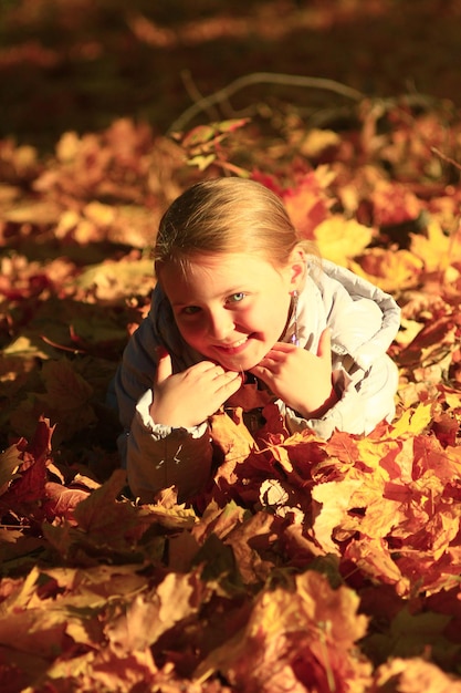 niña tendida en hojas amarillas en el parque de otoño