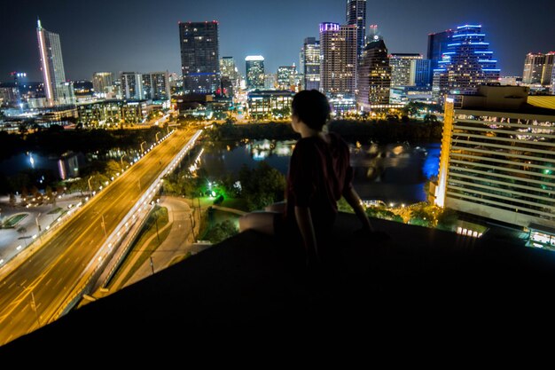 Foto niña en la terraza mirando el paisaje urbano iluminado