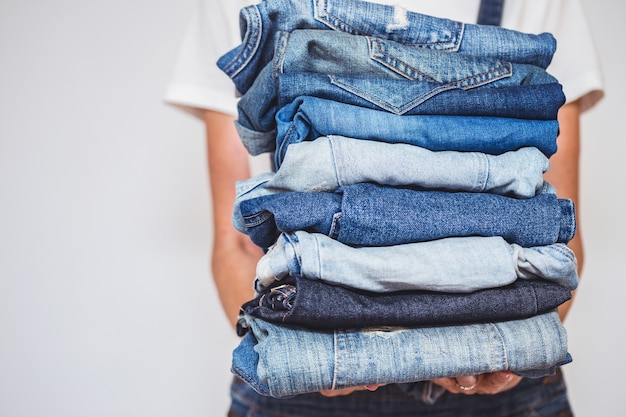 La niña tiene una pila de jeans en sus manos. limpieza en el armario.