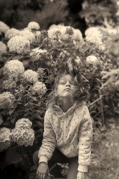 Foto niña tirando el cabello mientras se arrodilla contra las flores en el parque