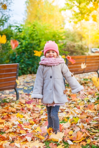 Niña tirando hojas en el parque de otoño