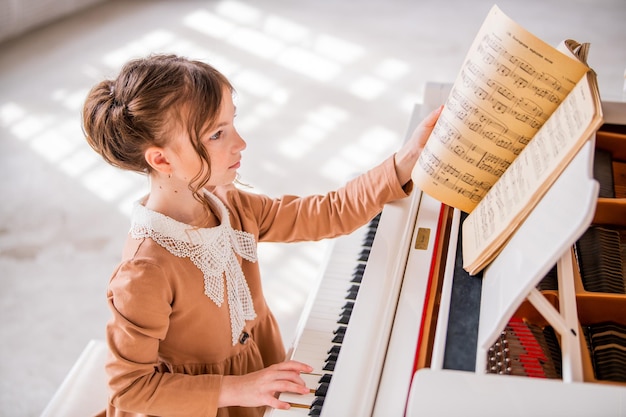 Una niña toca un gran piano blanco en una habitación luminosa y soleada