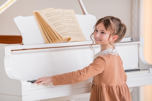 Una niña toca un gran piano blanco en una habitación luminosa y soleada