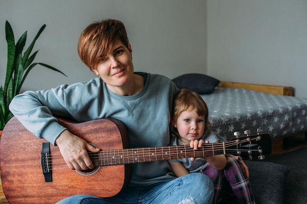 La niña toca la guitarra con su madre en el suelo en casa