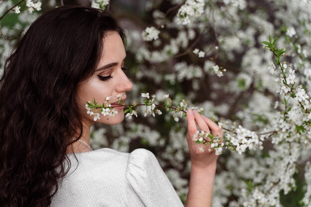 Niña toca y huele una rama de un árbol de flores blancas sin máscara médica. Primavera caminando en el parque.