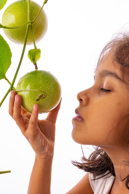 Una niña tocando la fruta de la pasión verde fresca en la vid con fondo blanco aislado