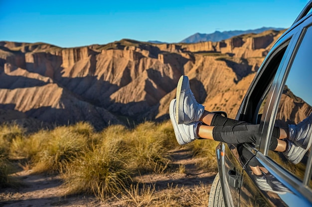 Niña tocando sus pies a través de la ventana del auto en medio de un paisaje desértico