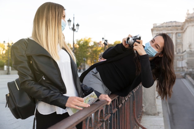 Una niña tomando una foto de su amiga con una cámara analógica. Ambos llevan máscaras faciales. Concepto de nueva normalidad.