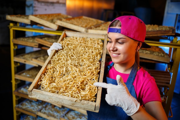 La niña trabaja en la producción de espaguetis. Hacer fideos. Fábrica de pasta. Etapa de producción de pasta. Tallarines crudos. Trabajador con una caja de pasta.