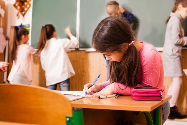 Una niña trabajadora está trabajando en su tarea durante el freno mientras otros niños juegan juntos