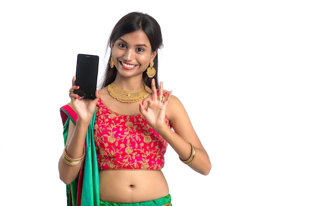 Niña tradicional india joven que usa un teléfono móvil o un teléfono inteligente y muestra un teléfono inteligente con pantalla en blanco