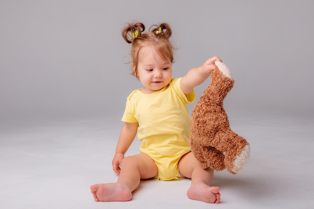 Una niña con un traje amarillo se sienta y juega con un oso de peluche en un fondo blanco