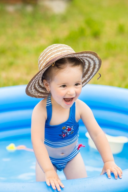 Niña en traje de baño jugando y nadando en una piscina inflable en un césped en el jardín