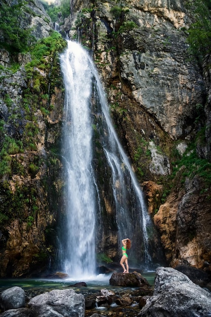 Una niña en traje de baño verde se encuentra bajo los arroyos de la cascada Grunas Waterfall es un sitio pintoresco dentro del Parque Nacional de Thethi Albania