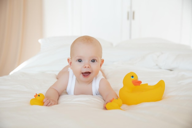 Una niña con un traje blanco acostada en la cama jugando con patitos de goma