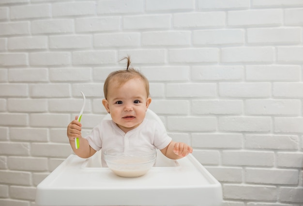 niña en un traje blanco está sentada en una silla de alimentación con una cuchara