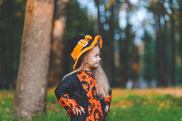 Niña en traje de bruja se encuentra en el parque en otoño el día de fiesta de Halloween.