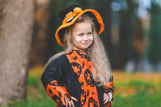 Niña en traje de bruja se encuentra en el parque en otoño el día de fiesta de Halloween.