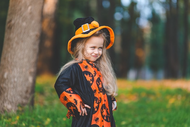 Niña en traje de bruja se encuentra en el parque en otoño el día de fiesta de Halloween.