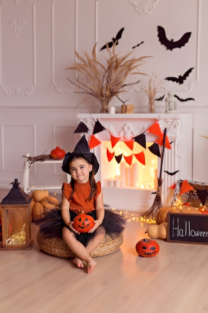 niña en traje de bruja de halloween con calabazas