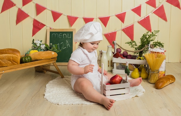 Niña en un traje de chef se sienta con fruta