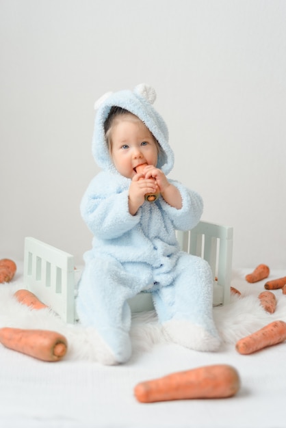 Niña en un traje de conejo comiendo zanahorias.