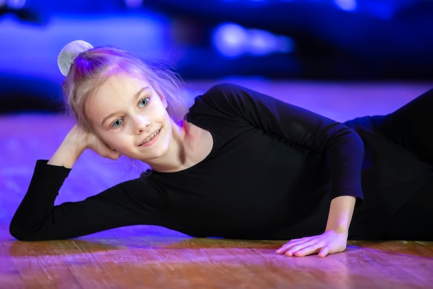 Una niña con traje de gimnasia yace en el suelo y mira a la cámara.