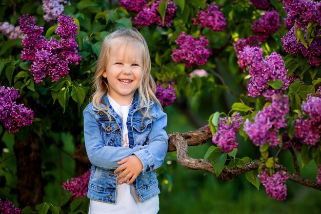 Niña en un traje de mezclilla camina en el jardín lila en la primavera