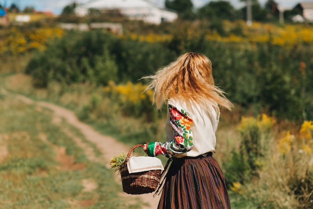 Una niña en un traje nacional y con una canasta de flores camina sobre un campo verde Traje nacional