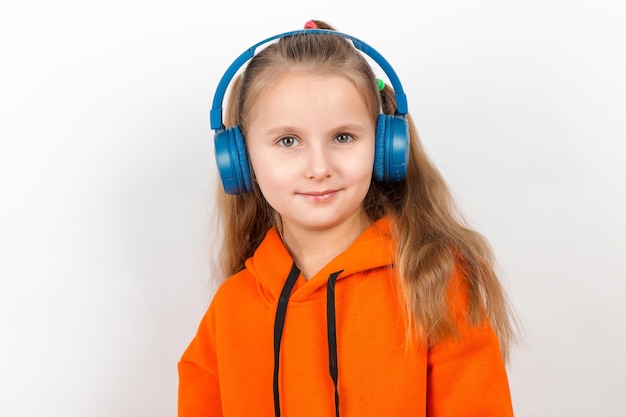 Una niña con traje naranja escuchando música con auriculares azules de fondo blanco