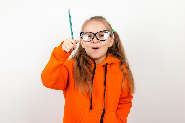 Una niña con traje naranja, gafas y lápiz El concepto de autodesarrollo de la formación escolar Sobre un fondo blanco