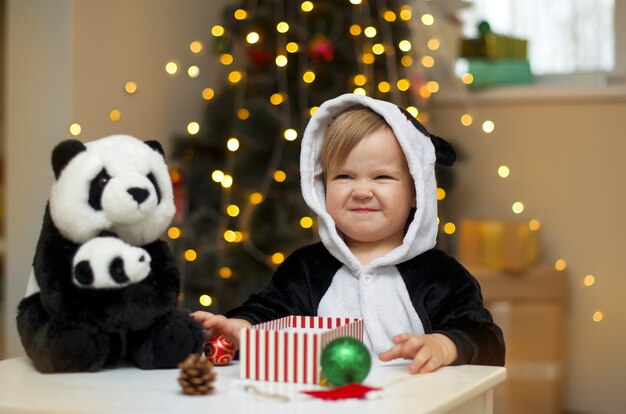 Niña en un traje de panda con juguete de panda abierto regalo de Navidad bajo el árbol de Navidad