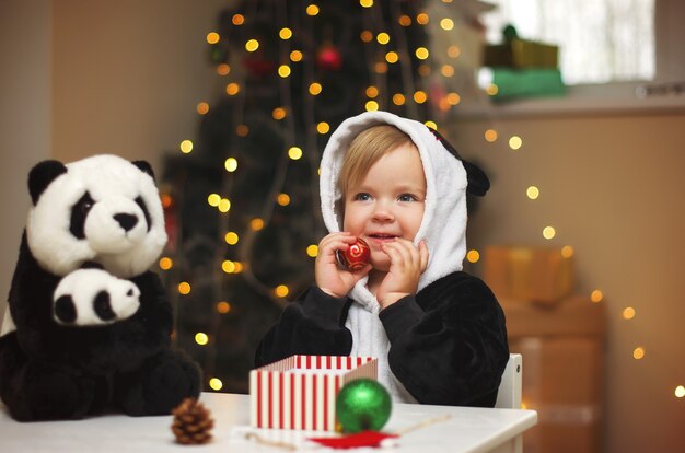 Niña en un traje de panda con juguete de panda abierto regalo de Navidad bajo el árbol de Navidad