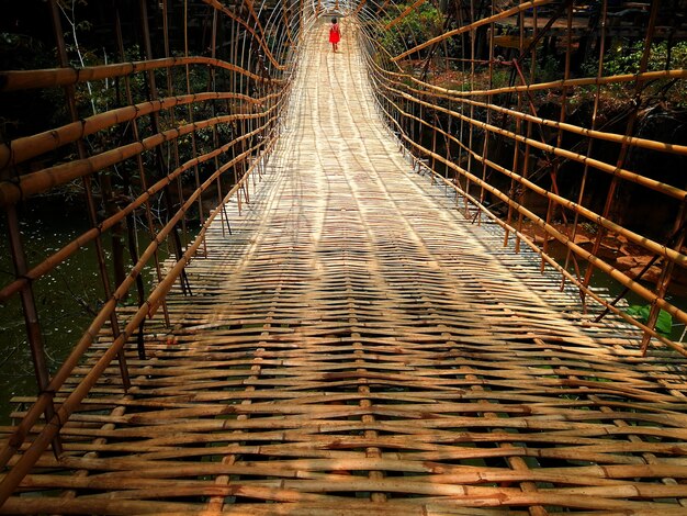 Foto una niña con traje rojo caminando por el puente de bambú