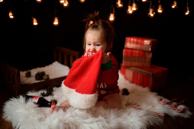 Niña en un traje rojo de Navidad con guirnaldas retro se sienta sobre una piel