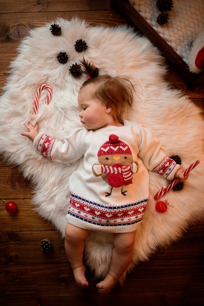 Niña en un traje rojo de Navidad con guirnaldas retro se sienta sobre una piel