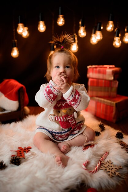 Niña en un traje rojo de Navidad con guirnaldas retro se sienta sobre una piel