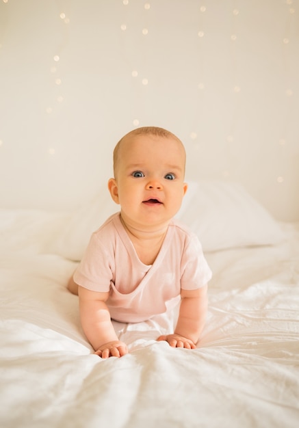 Niña en traje rosa se arrastra en la cama