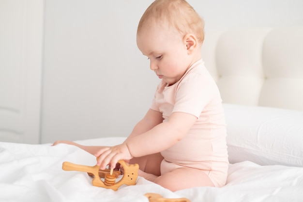 Niña en traje rosa claro jugando con juguetes de madera en ropa de cama blanca en la cama