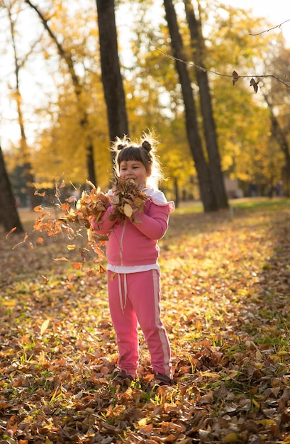 Una niña con traje rosa sosteniendo hojas en el parque de otoño