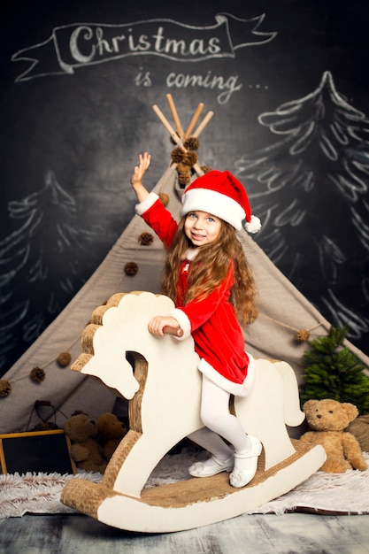 Niña en traje de Santa en un caballito está listo para celebrar las fiestas.