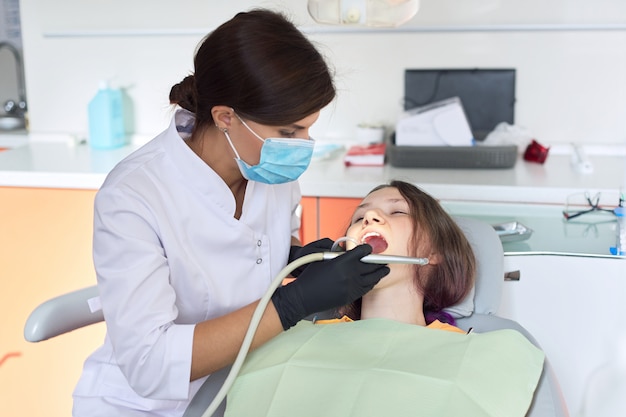 Niña tratando dientes, adolescente femenino sentado en la silla de dentistas