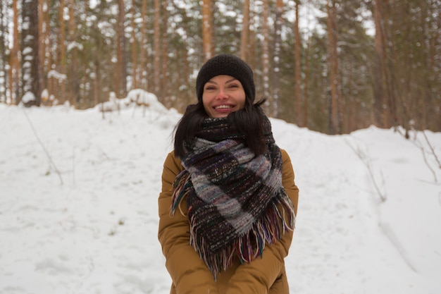 Una niña traviesa con una chaqueta marrón y un sombrero negro se encuentra en medio del bosque de invierno sonriendo