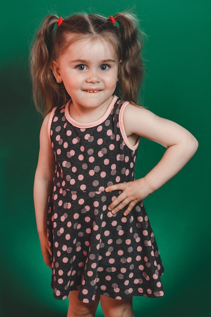 Niña de tres años con colas en vestido posando en estudio sobre fondo verde 2021