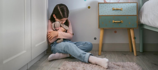 Niña triste abrazando juguete de peluche sentado en el suelo