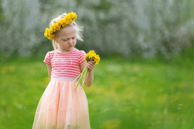 Foto niña triste en el campo verde con diente de león amarillo pequeña dama en vestido rosa sostiene flores enfoque selectivo