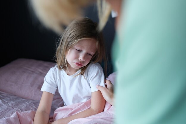 Niña triste se despertó y está sentada en la cama, primer plano. Pobre bienestar físico del niño, miedo ansiedad resentimiento